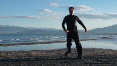 Siyah takım elbiseli sporcu yaz akşamı göl kıyısında antrenman yapıyor.