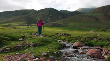 Genç kadın turist, pitoresk dağ vadisinde derede yürüyor.