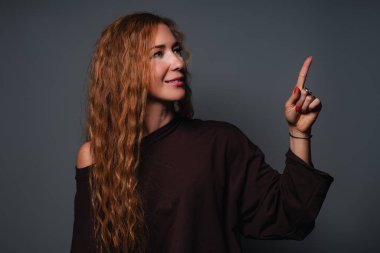 Gri arkaplanda portresi olan genç bir kadın işaret ediyor.