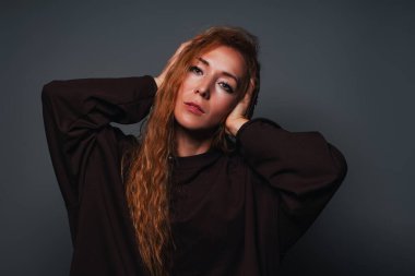 Genç bir kadın gri arka planda duygusal portre takıyor.