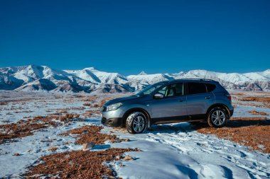 Kırgızistan - 02 Ocak 2025: Nissan Kashqai arabası kış günü yüksek dağların arka planında duruyor