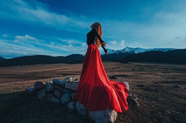 Yüksek dağlarda poz veren kırmızı elbiseli güzel bir kadın.