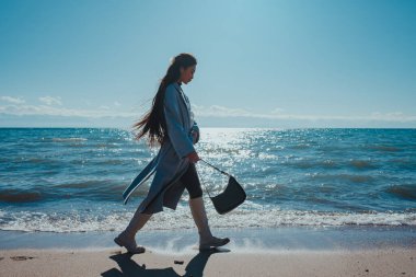 Genç ve şık bir kadın yaz günü deniz kıyısında yürüyor.