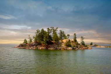 Killarney İl Parkı, Ontario, Kanada 'daki berrak su gölünde ağaçları olan uzak Red Granite Adası.
