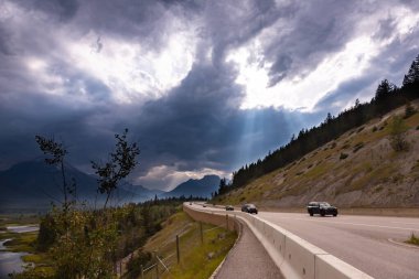 Kanadalı Rocky Dağları, Yaz Günbatımı, Banff Area, Alberta, Kanada arasında, Güneş ışınlarıyla gölün yakınındaki karayolunu aydınlatan dramatik gökyüzü