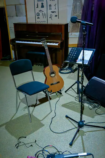 An image of an acoustic guitar stands on stage near a music stan