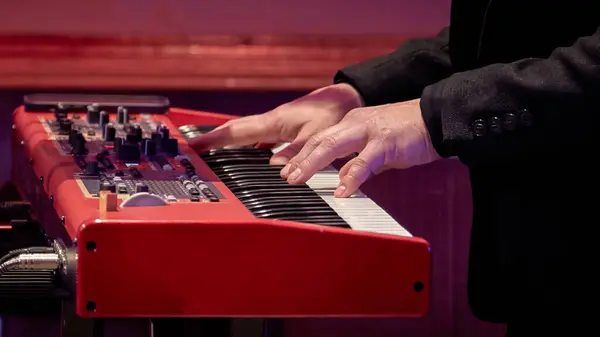 Image of a musician's hand on the keys of a red electrode piano