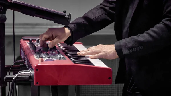 Image of a musician's hand on the keys of a red electrode piano