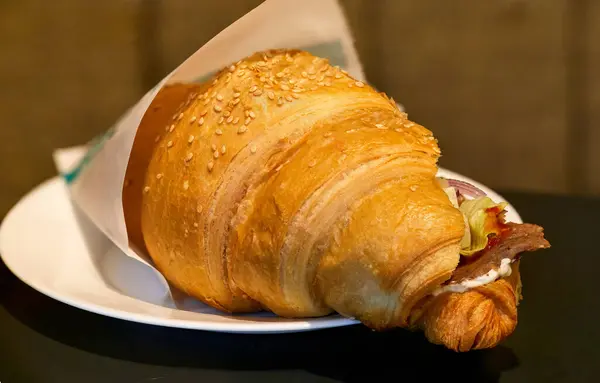 一个美味的羊角面包与火腿和洋葱放在盘子里的图像 图库图片