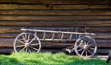 Bahçedeki ahşap bir Ukrayna evinin yanında duran büyük tekerlekleri olan eski ahşap bir at arabası.