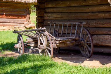 Bahçedeki ahşap bir Ukrayna evinin yanında duran büyük tekerlekleri olan eski ahşap bir at arabası.