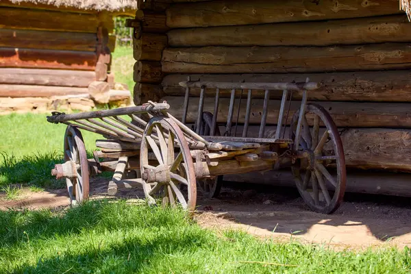 Bahçedeki ahşap bir Ukrayna evinin yanında duran büyük tekerlekleri olan eski ahşap bir at arabası.
