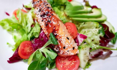 Grilled salmon fish fillet in sesame seeds and fresh vegetable salad with cherry tomatoes, lettuce and avocado slices closeup. Healthy food concept.