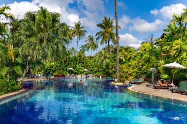 THAILAND, PHUKET, FEBRUARY, 2023: Swimming pool among a beautiful garden with tall palm trees on the territory of Patong Merlin Hotel in Phuket, Thailand