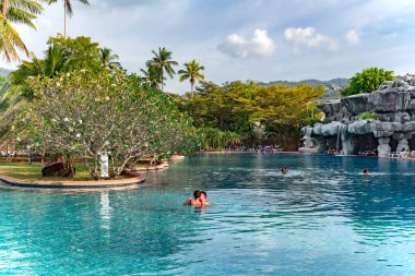THAILAND, PHUKET, FEBRUARY, 2023: Tayland 'ın Phuket kentindeki Duangjitt Resort & Spa bölgesinde uzun palmiye ağaçları olan güzel bir bahçede yüzme havuzu