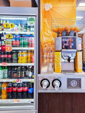 LATVIA, RIGA, APRIL, 2023 - Portakal suyu makinesindeki taze portakal meyveleri paket servis için plastik şişeler ve çeşitli meşrubatlarla dolu bir buzdolabı. Teslimat konseptini kaldır.
