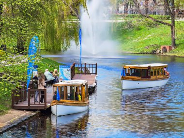 LATVIA, RIGA, APRIL, 2023: Letonya 'nın başkenti Riga' daki Bastion Hill yakınlarındaki şehir çeşmesinin arka planında keyif botları olan rıhtım. AB