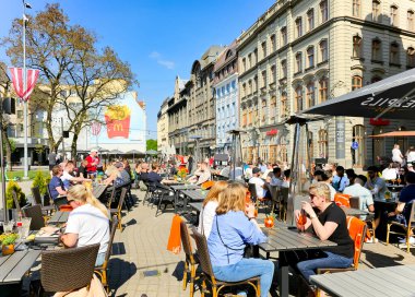 LATVIA, RIGA, MAYIS, 2023: İnsanlar Riga Old Town 'daki Livu Meydanı' ndaki kafelerin açık verandasında yemek yiyorlar. - Letonya. Riga şehir tarihi merkezi UNESCO 'nun Dünya Mirasları Alanıdır.