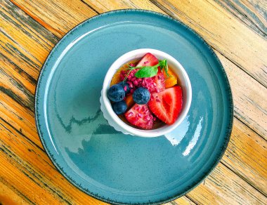 Sarı ahşap bir masanın arka planında mavi bir tabakta taze yaz meyveli ev yapımı tatlı. Kremalı meyve tatlısı kavramı.