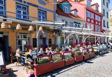 LATVIA, RIGA, MAYIS, 2023: Turistler Livu Meydanı 'ndaki en ünlü ve güzel meydanlardan birinin açık verandasında yemek yiyorlar..