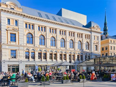LATVIA, RIGA, 15 Haziran 2023: Turistler Riga 'daki en ünlü ve en güzel meydanlardan biri olan Livu Meydanı' ndaki bir restoranın açık verandasında yemek yiyorlar.