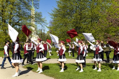 LATVIA, RIGA, 10 Mayıs 2023: Letonya 'nın başkenti Riga Old Town' da Özgürlük Bulvarı 'ndaki Özgürlük Anıtı' nın yanında ellerinde küçük bayraklarla prova yapan neşeli renkli kostümlü genç dansçılar. AB. 