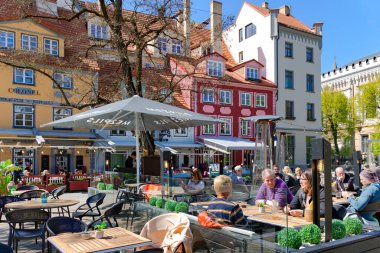 LATVIA, RIGA, 10 Mayıs 2023: Turistler Livu Meydanı 'ndaki en ünlü ve en güzel meydanlardan birinin açık verandasında yemek yiyorlar..