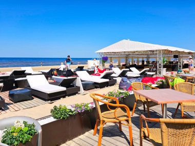 LATVIA, JURMALA, 25, HAZİRAN, 2023: Hasır mobilyalı açık hava kafe ve Baltık kıyısındaki Majori 'de bronzlaşmak için beyaz yumuşak güneş şezlongları. Letonya. 