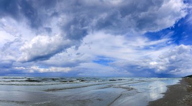 Letonya, Jurmala 'daki Baltık Denizi' nin üzerindeki yemyeşil kümülüs bulutları. Doğa konsepti. Kümülüs bulutları fırtınaya dönüşür. Dalgalar kıyıya vurdu ve bulutlar suya yansıdı..