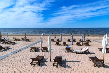 LATVIA, JURMALA, MAJORI, 18 HAZİRAN, 2023: Şemsiyelerle ahşap güneş şezlongları Jurmala, Letonya 'daki Baltık Denizi' nin temiz kumlu sahillerinde