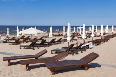 LATVIA, JURMALA, MAJORI, 18 HAZİRAN, 2023: Şemsiyelerle ahşap güneş şezlongları Jurmala, Letonya 'daki Baltık Denizi' nin temiz kumlu sahillerinde