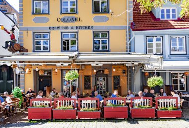 LATVIA, RIGA, 12, AUGust, 2023: Turistler, Riga 'daki en ünlü ve güzel meydanlardan biri olan Livu Meydanı' ndaki bir Albayın açık verandasında yemek yiyorlar..