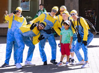 LATVIA, RIGA, 12, AĞUSTOS, 2023: Minyonlar gibi giyinmiş bir grup neşeli adam, Letonya 'nın Riga Eski Kasabası' nda çocuklarla fotoğraf çekiyor.