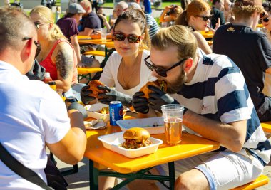 LATVIA, RIGA, 15, AUGust, 2023: İnsanlar Riga şehir parkındaki kafenin açık verandasında birayla hamburger yiyorlar