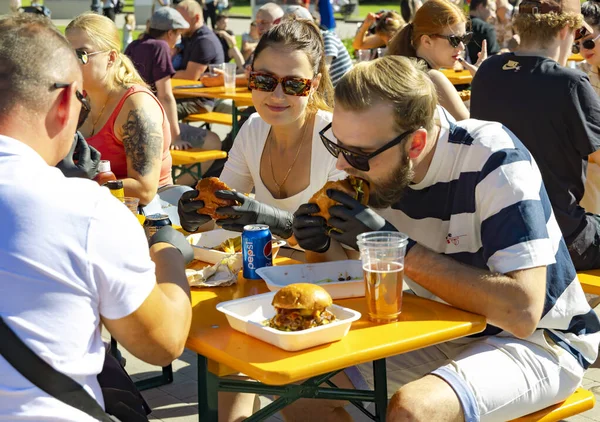 ラトビア August 2023 人々はラトビアのリガ市立公園のカフェのオープンベランダでビールでハンバーガーを食べる ロイヤリティフリーのストック画像