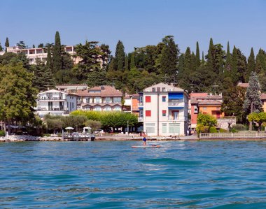 İtalya, LOMBARDY, COMO, 25 AĞUSTOS, 2023: İnsanlar Como Gölü 'nde yüzüyorlar şehir mimarisinin ve İtalyan Alplerinin arka planına karşı. Kuzey İtalya 'da Lombardiya Bölgesi. 