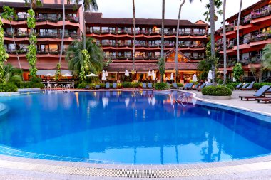 THAILAND, PHUKET, 18, FEBRUARY, 2023: Akşamları Patong Merlin Oteli 'nin bölgesinde uzun palmiye ağaçları olan güzel bir bahçede yüzme havuzu, Phuket, Tayland