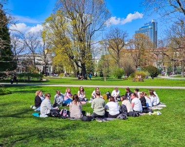 LATVIA, RIGA, 23, APRIL, 2024: Bir grup genç arkadaş Riga, Letonya 'da sıcak bir bahar gününde Vermanes Park' taki yeşil çimlerde oturuyorlar