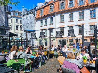 LATVIA, RIGA, 01, MAYIS, 2024: Riga Old Town 'daki kafelerin açık verandasında öğle yemeği yiyen insanlar. - Letonya. Riga şehir tarihi merkezi UNESCO 'nun Dünya Mirasları Alanıdır.