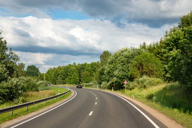 LATVIA, RIGA, 05, HAZİRAN, 2024: Riga banliyöleri, Letonya 'da mavi gökyüzü ve bulutlara karşı ormanlar arasında asfalt yol