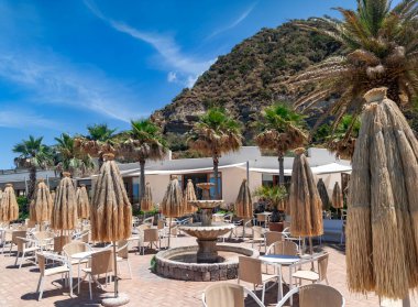 İtalya 'nın Ischia adasındaki dağların eteğinde masalı ve saman şemsiyeli bir restoranın verandası.