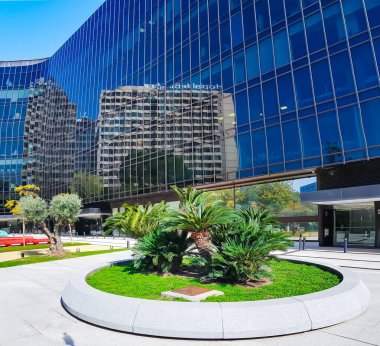 İspanya, BARCELONA, MARCH, 25, 2021: Ön cephesinde koyu cam paneller olan modern ofis binası ve İspanya 'nın Barcelona kentinin avlusunda kırmızı bankları olan güzel bir bahçe