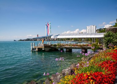 SWitzERLAND, MONTREUX, AĞUSTOS, 15, 2021: Leman Gölü veya Cenevre Gölü üzerinde gemi ve çiçekler için İsviçre 'nin Montreux kentinde kıyı şeridi boyunca yer alan iskele manzaralı panorama manzarası