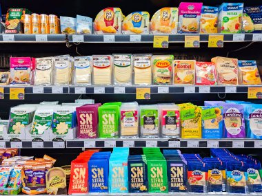 Letonya, Riga, 23 Haziran 2024: Farklı üreticilerin çeşitli peynirleri ve Riga, Letonya 'daki alışveriş merkezinde bir peynir dilimleme makinesi bulunan raflar.