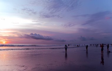 BALI, INDONEZYA, AĞUSTOS, 18, 2021: İnsanlar sahilde fotoğraf çekiyor ve Endonezya 'nın Bali kentindeki Hint okyanusunda inanılmaz renkli günbatımının tadını çıkarıyorlar. Renkli doğa deniz göğü. Doğa. Seyahat kavramı.