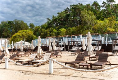 Şemsiyeli ahşap güneş şezlongları ve Jurmala, Letonya 'da Baltık Denizi kıyısında beyaz perdeli çardaklar.