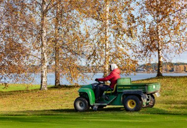 LATVIA, RIGA, 25, ECTOBER, 2024: Bir golf kulübü çalışanı Riga, Letonya 'daki Kisezers gölünün kıyısındaki oyun alanlarını korumak için bir iş aracı kullanıyor.