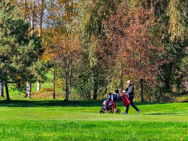 LATVIA, RIGA, 25, OCTOBER, 2024: Bir golfçü ekipmanlarıyla birlikte Riga, Letonya 'daki Kisezers gölünün kıyısındaki karışık ormanın yakınındaki bir golf kulübüne gider..