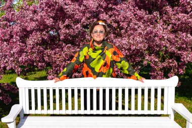 Parlak ceketli güzel bir kadın bahçedeki kiraz çiçeklerinin tadını çıkarıyor. Doğanın güzelliği kavramı.