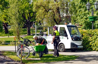 LATVIA, RIGA, HAZİRAN, 21, 2025: Belediye park bakım işçileri Letonya 'nın Riga kentindeki beyaz elektrikli araçlarında çöp topluyorlar.